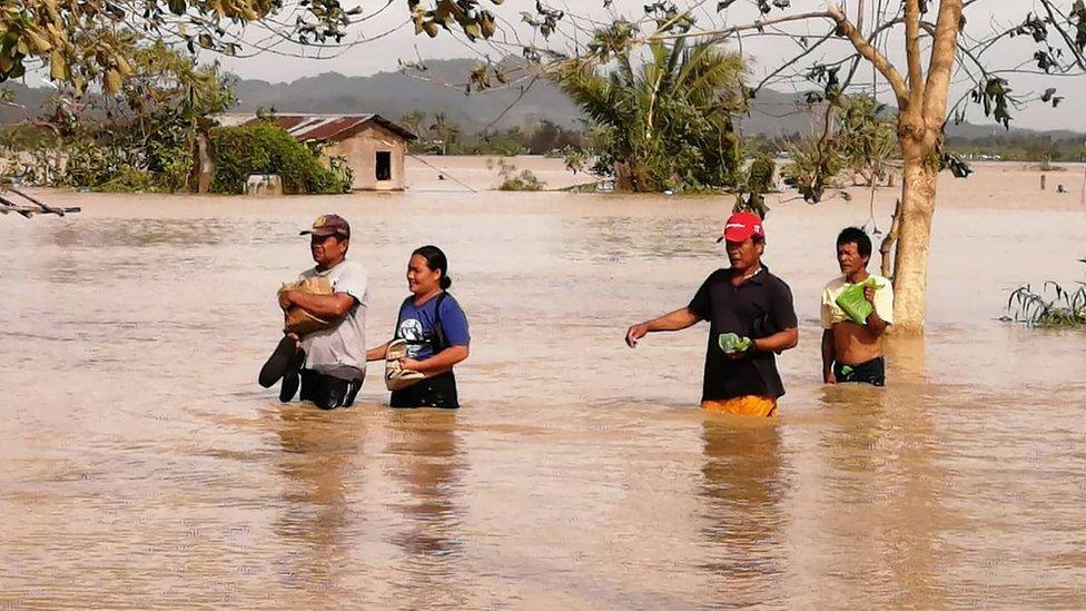 Residents wade through a flooded highway, caused by heavy rains due to typhoon Phanfone, in Ormoc City