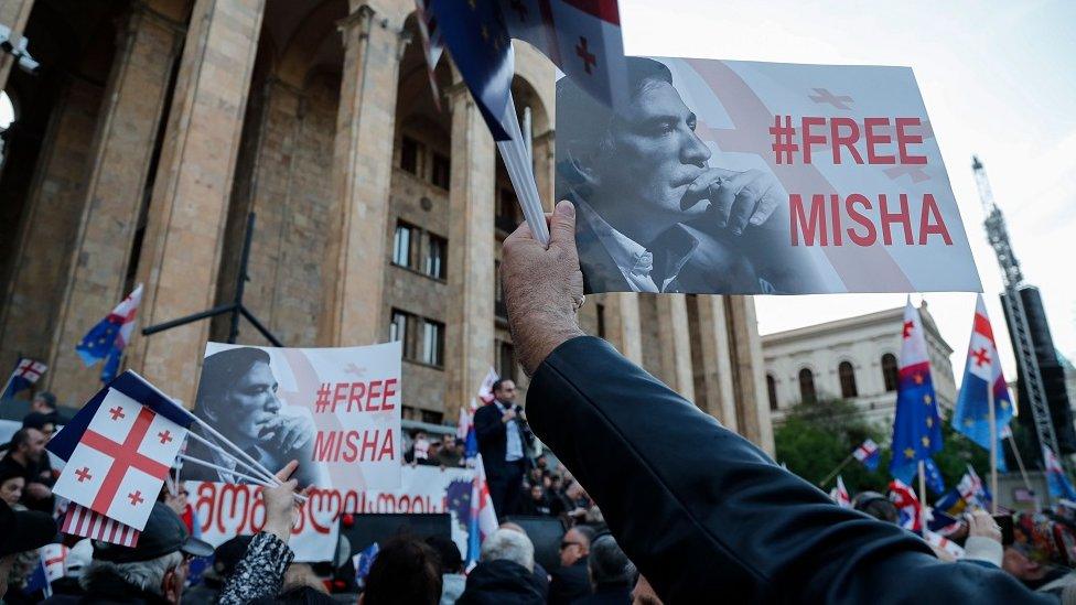 People at an anti-government rally outside the Georgian parliament building hold placards showing the face of jailed former president Mikheil Saakashvili