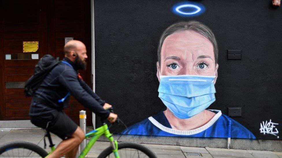 man cycling past graffiti of NHS worker