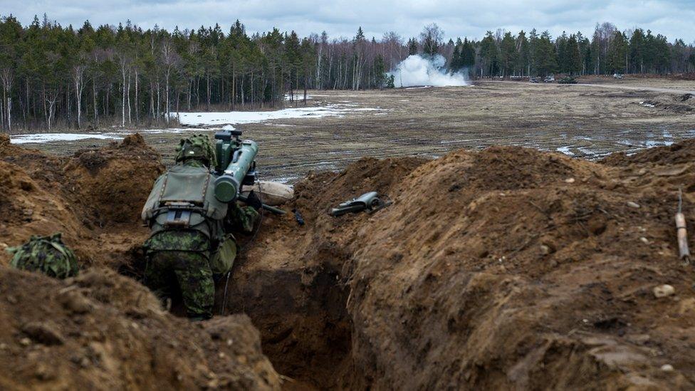 Soldier firing from a trench, with smoke in the distance