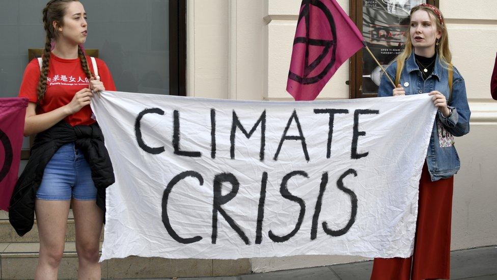 Extinction Rebellion activists hold a banner and a placard outside the Royal Opera House main entrance during a protest in London