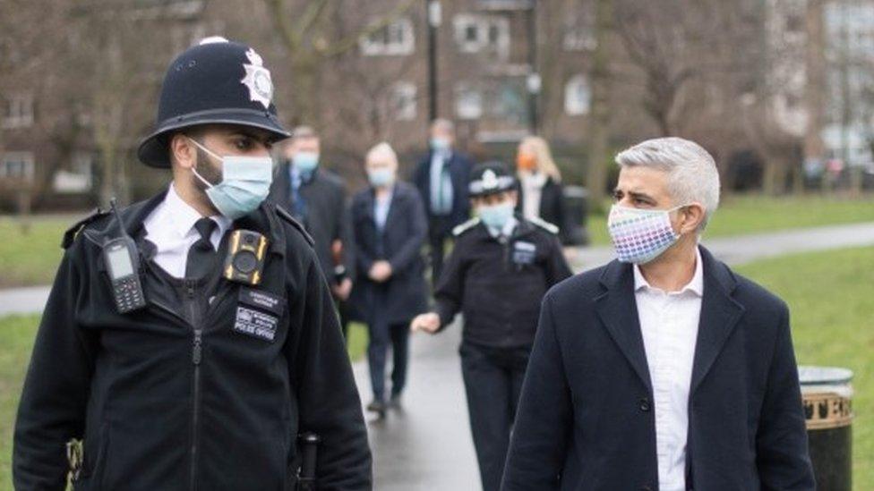 A police officer talks to Sadiq Khan while walking through a park