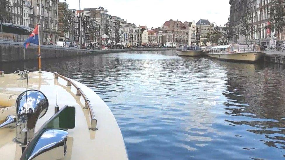 Prow of Prinses Irene sailing down canal with cityscape in background