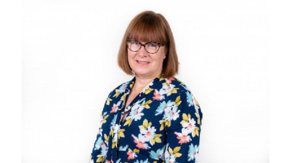 Woman with medium-length brown hair and glasses wearing a flowery dress