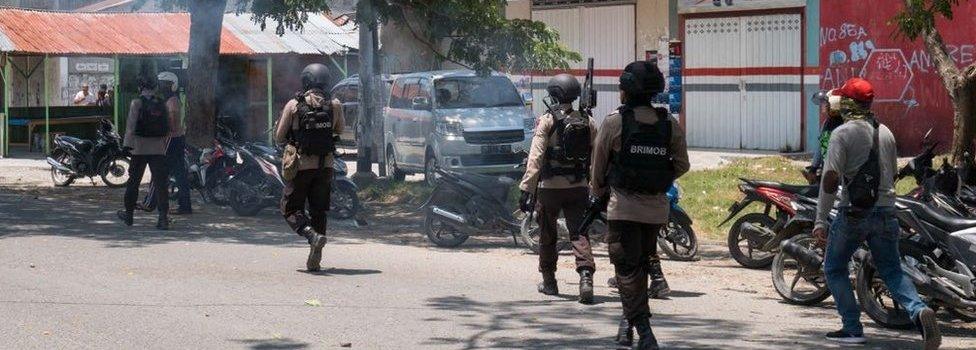 Police fire warning shots outside a shop in Palu, Indonesia