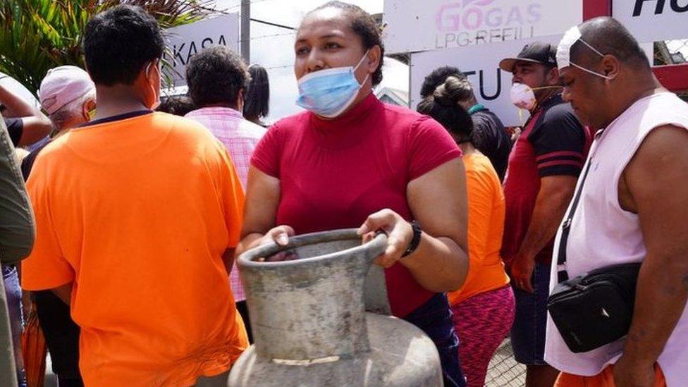 A woman (C) carries a refilled gas container in the centre of the capital Nuku'alofa ahead of the country's first lockdown on February 2, 2022, after Covid-19 was detected in the previously virus-free Pacific kingdom as it struggles to recover from the deadly January 15 volcanic eruption and tsunami.