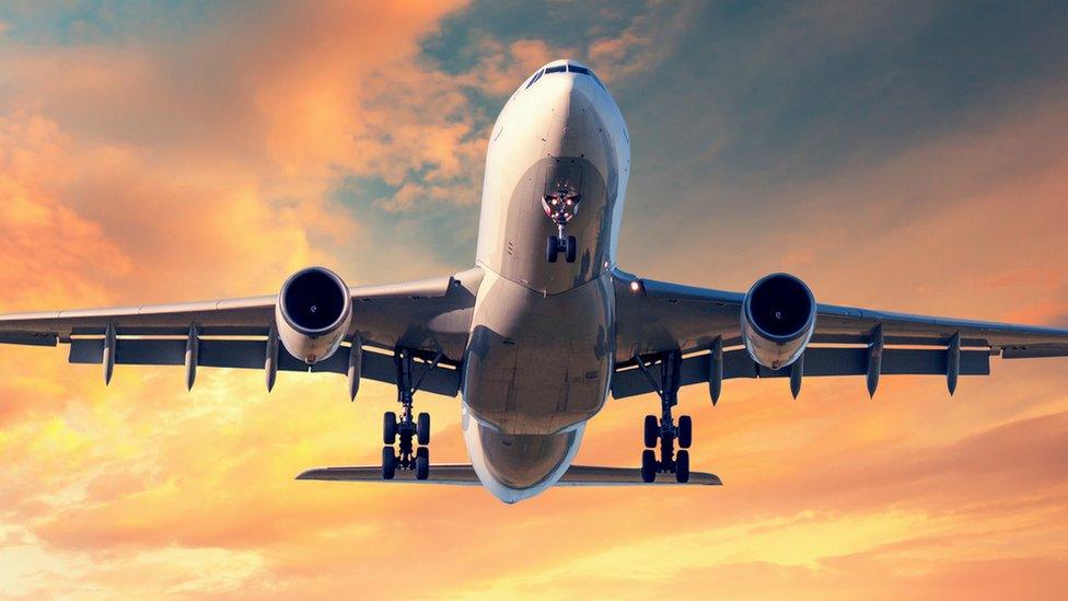 A plane descends beneath sunset-lit clouds