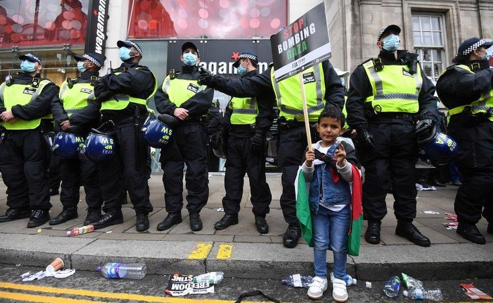 A young Palestine supporter carries a placard in front of riot police during a demonstration outside the Israeli embassy