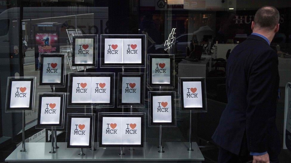 A man passes a display of "I love MCR" signs in the window of an estate agent"s in Manchester