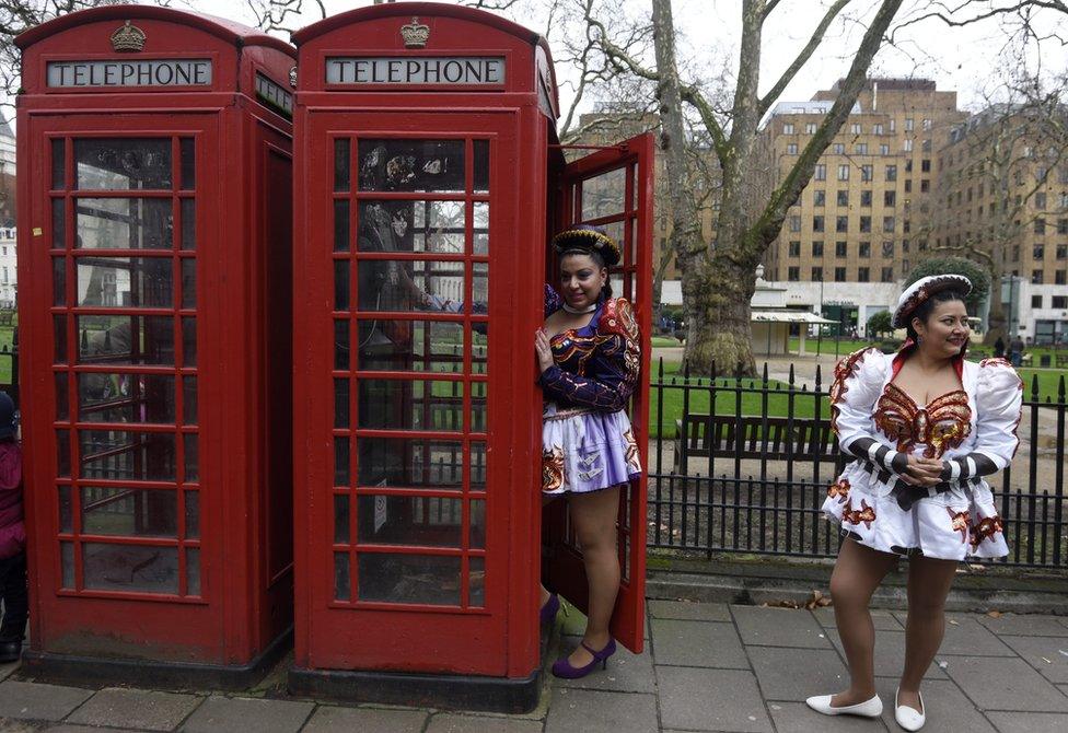 Members of the Caporal's San Simon Londres Latin American folk group stand by an old telephone box