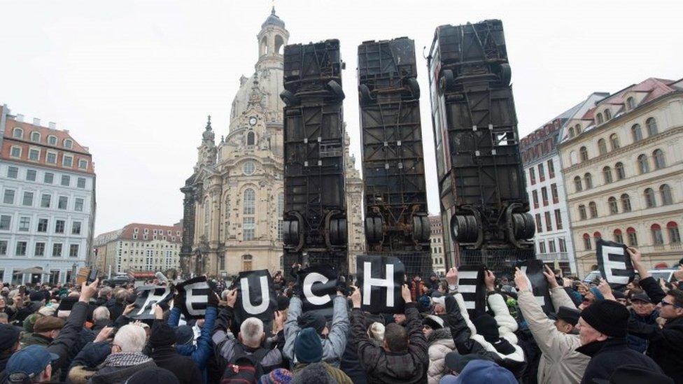 Demonstrators protest against the upturned buses sculpture in Dresden (07 February 2017)