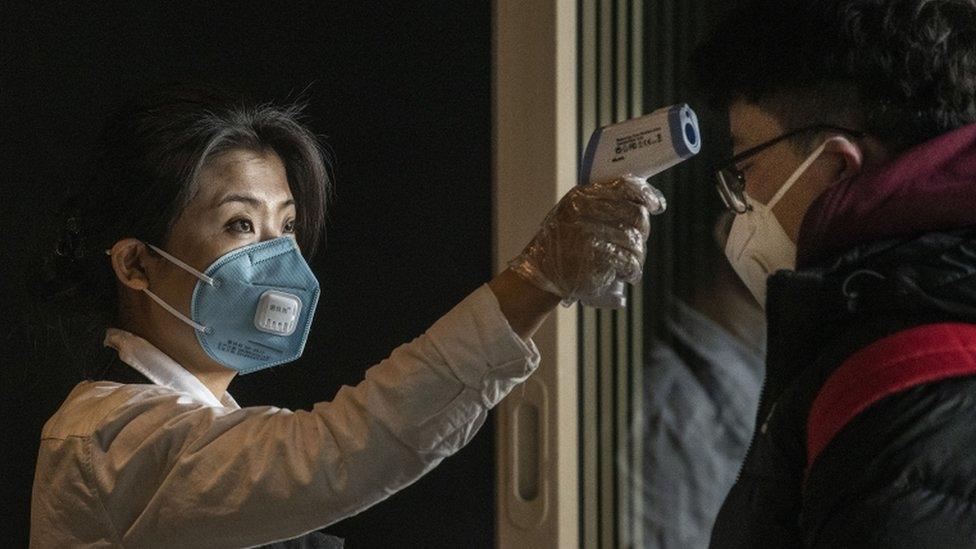 A Starbucks worker checks a customer's temperature at Beijing Capital Airport