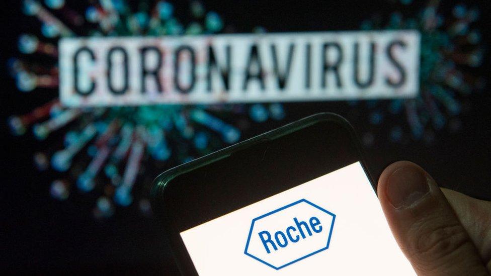 Roche logo seen displayed on a smartphone with a computer model of the COVID-19 coronavirus on the background