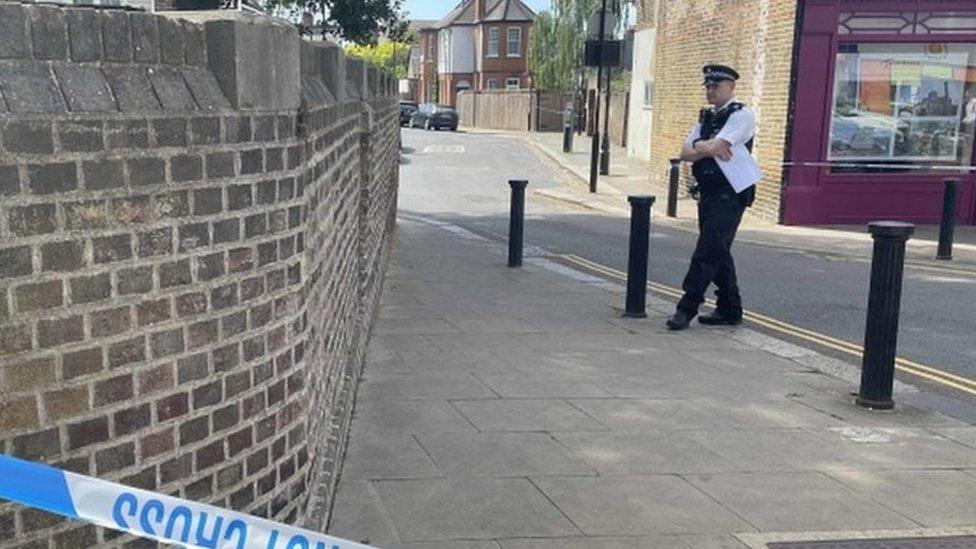 A police officer stands near the alleyway off Church Gardens, South Ealing