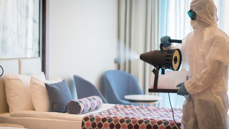 A man in a protective suit disinfecting a hotel room