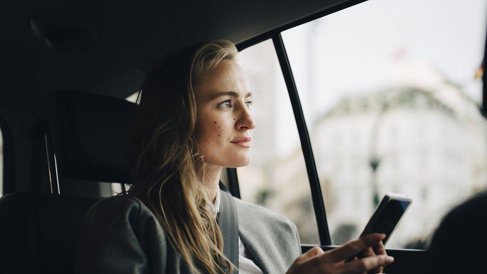 Woman with smart phone looking through window while sitting in taxi - stock photo