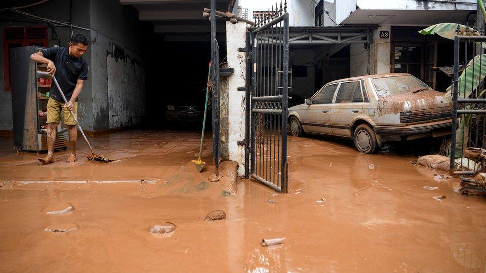 A man sweeps water and mud out of his home