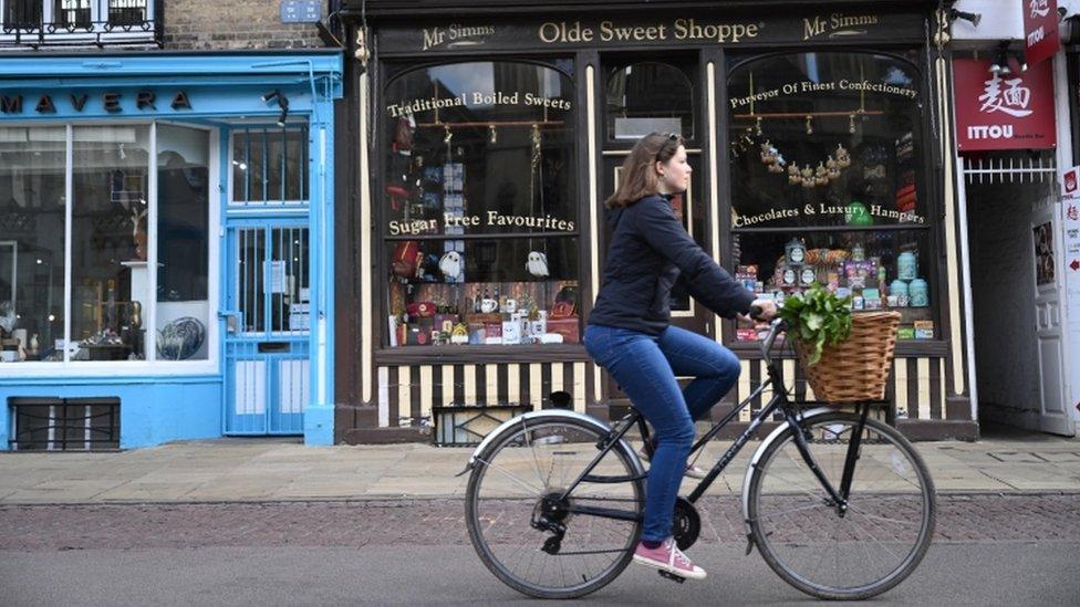 Woman cycling past small shops in Cambridge