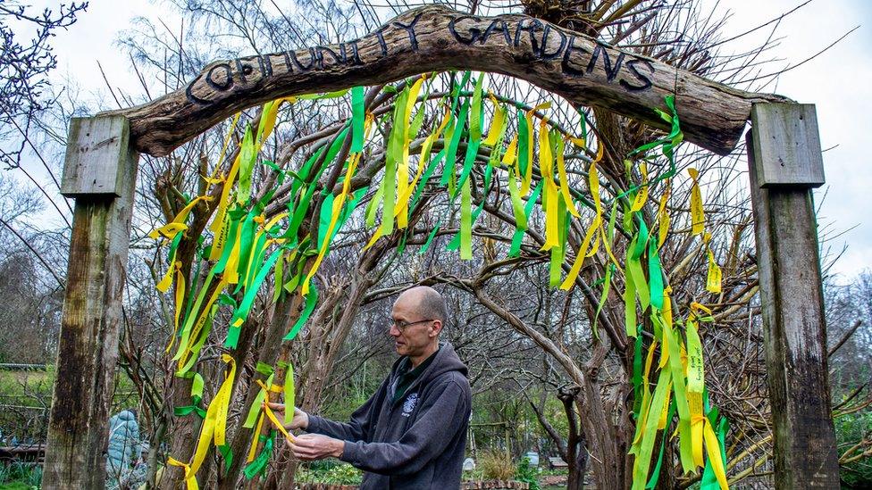 A man tying yellow and green ribbons to an archway at Windmill Hill City Farm in Bristol