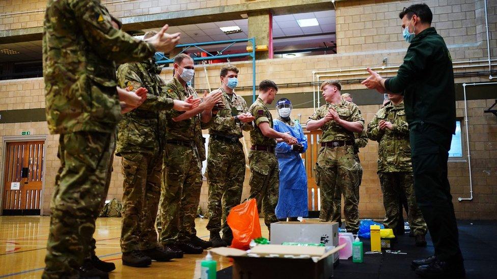 Military personnel stand over medical equipment on the ground as trainers talk them through how to use it.