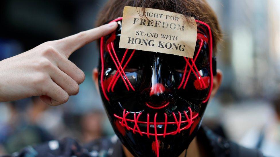 A masked anti-government protester points to a sign on his forehead which says "stand with freedom, stand with Hong Kong"