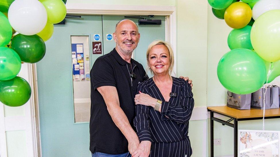 Adam and Many Gibbons leaning into each other surrounded by green and white balloons during the celebratory launch of the Mockingbird programme.