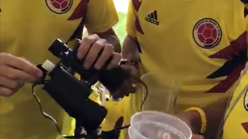 A close-up of the binoculars containing the alcohol being held by people wearing Colombia football shirts