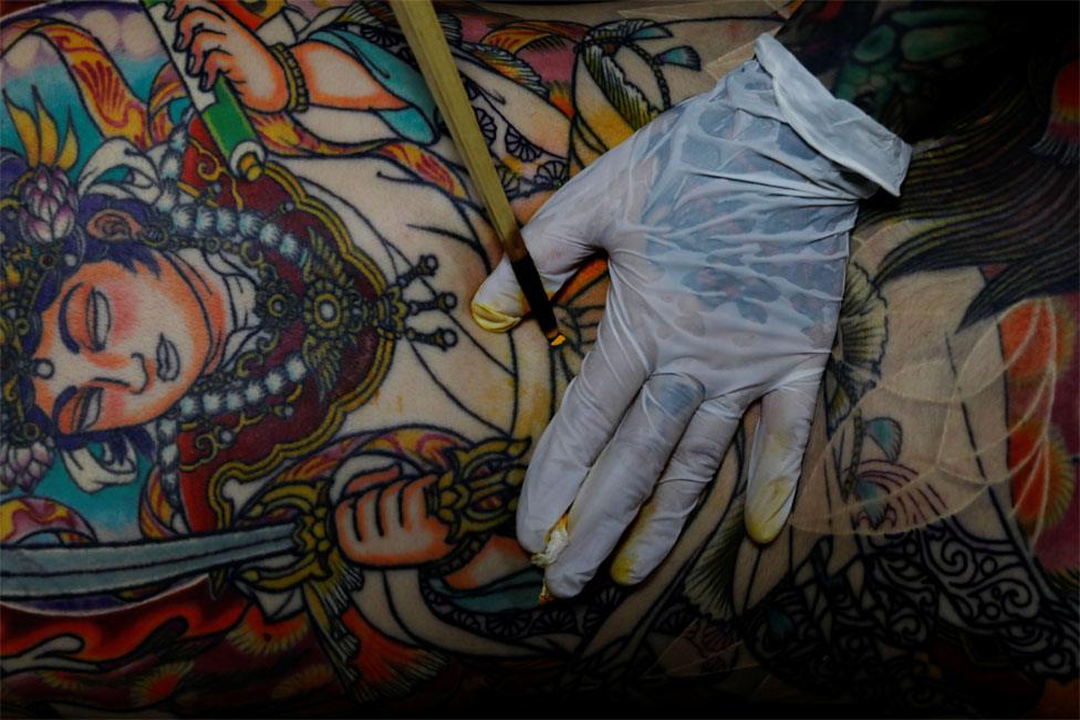 A tattoo artist works on a customer's back