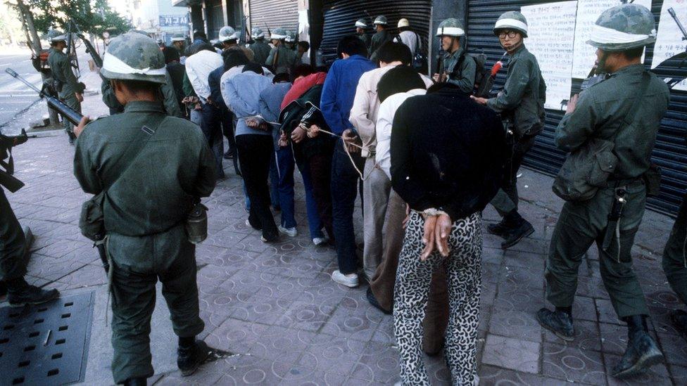 Protesters are tied together by their arms as troops look on