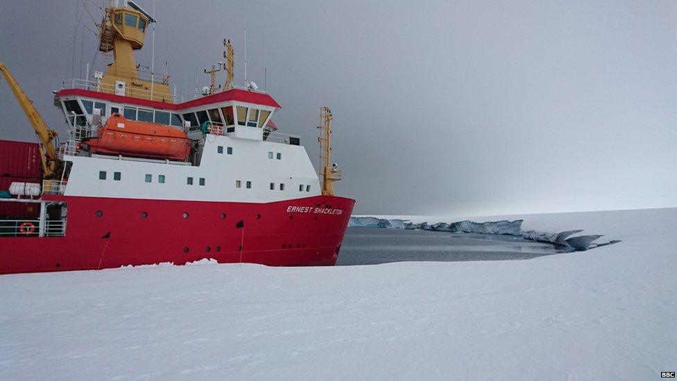 A large red and white ship moored against the white coast.