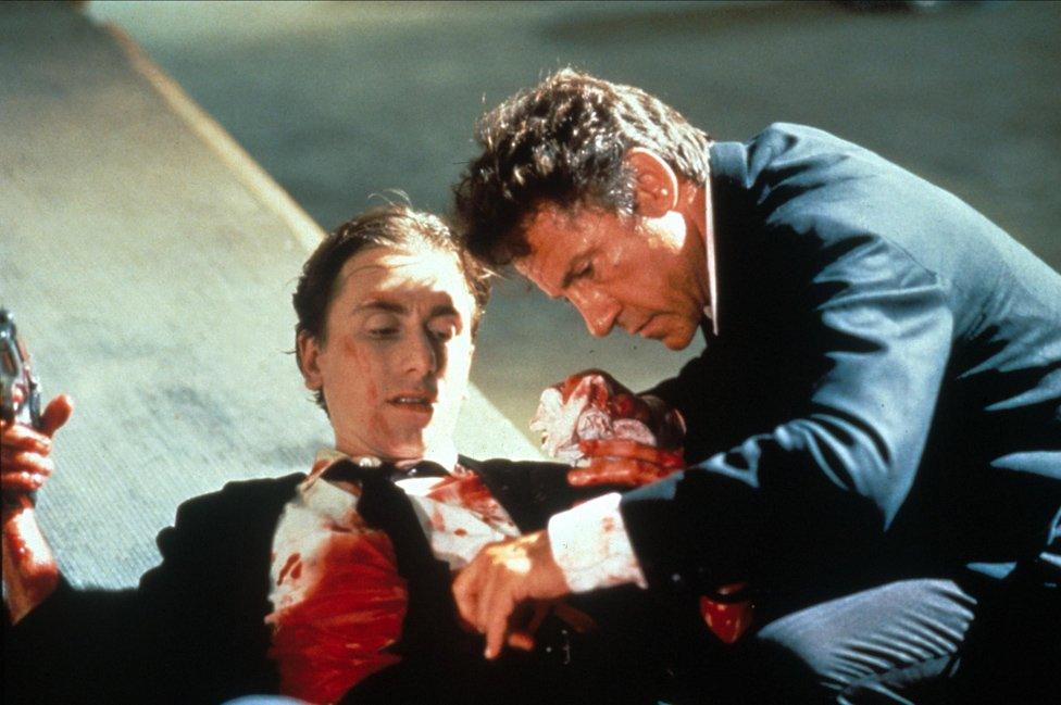 Tim Roth covered in blood and holding a gun is examined by Harvey Keitel