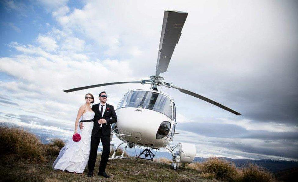 Kristy and Corey in the wedding outfits pose in front of a white helicopter