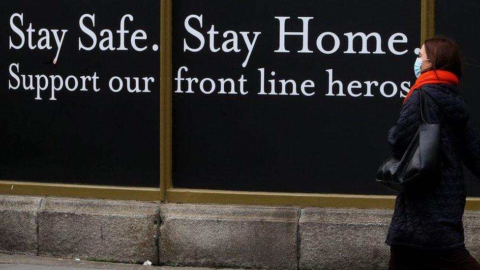 A woman walks past a shop hoarding which reads: "Stay safe. Stay home. Support our frontline heroes."