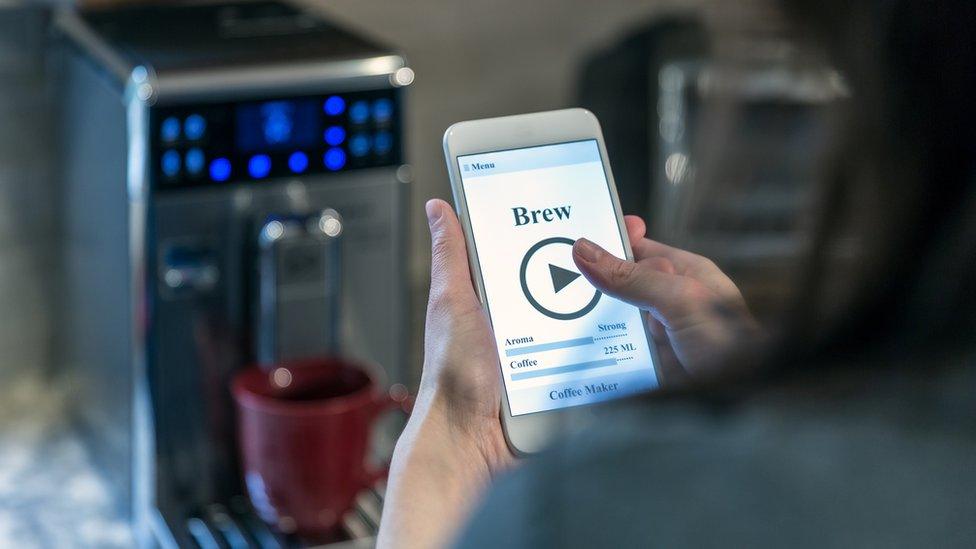 Woman operating coffee maker by smartphone