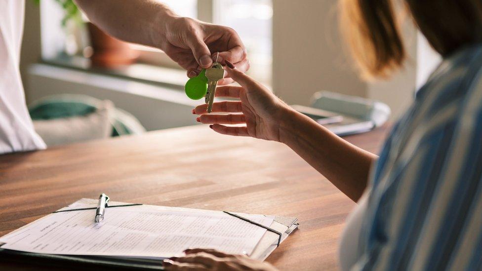 Stock photo of owner giving house keys to tenant after filling rental forms