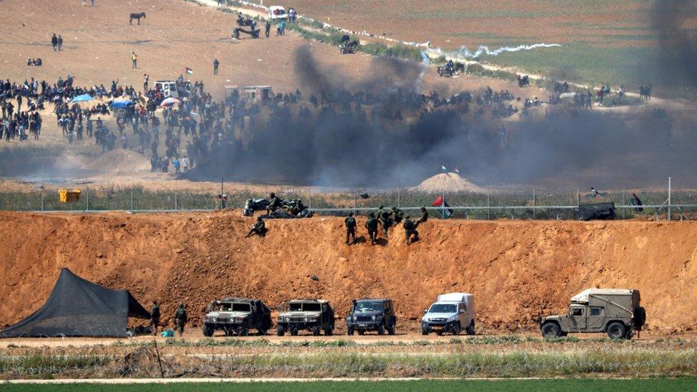 A picture taken from the southern Israeli kibbutz of Nahal Oz shows Palestinian men protesting on the other side of the border with Gaza (6 April 2018)