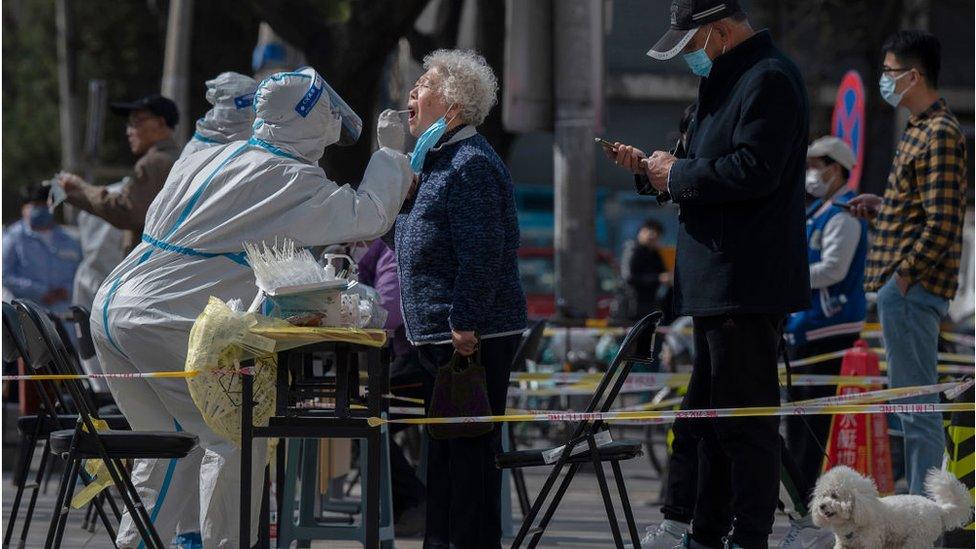 A health worker wears protective gear as she gives a nucleic acid test to detect COVID-19 on a local resident at a mass testing site after new cases were found, on April 6, 2022 in Beijing, China.