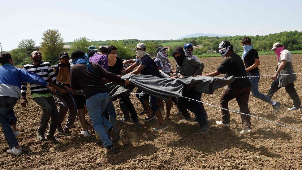 Migrants and refugees use blankets to pull razor wire from the border fence between Greece and Macedonia at the makeshift camp near the Greek village of Idomeni on April 13, 2016