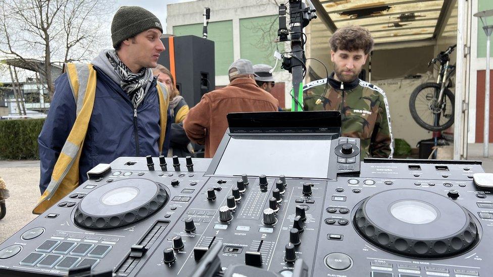 Two men stand looking at a bicycle with Dj decks on the front in Bristol