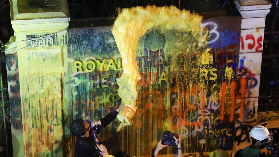 A demonstrator throws paint over a plaque with lettering on it in front of the police headquarters during a rally in Bangkok