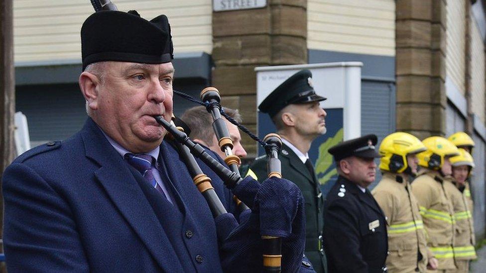 A piper plays as members of the emergency services stand at the service on Shankill Road