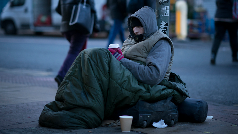 rough sleeper wrapped up in warm layers holding coffee cup