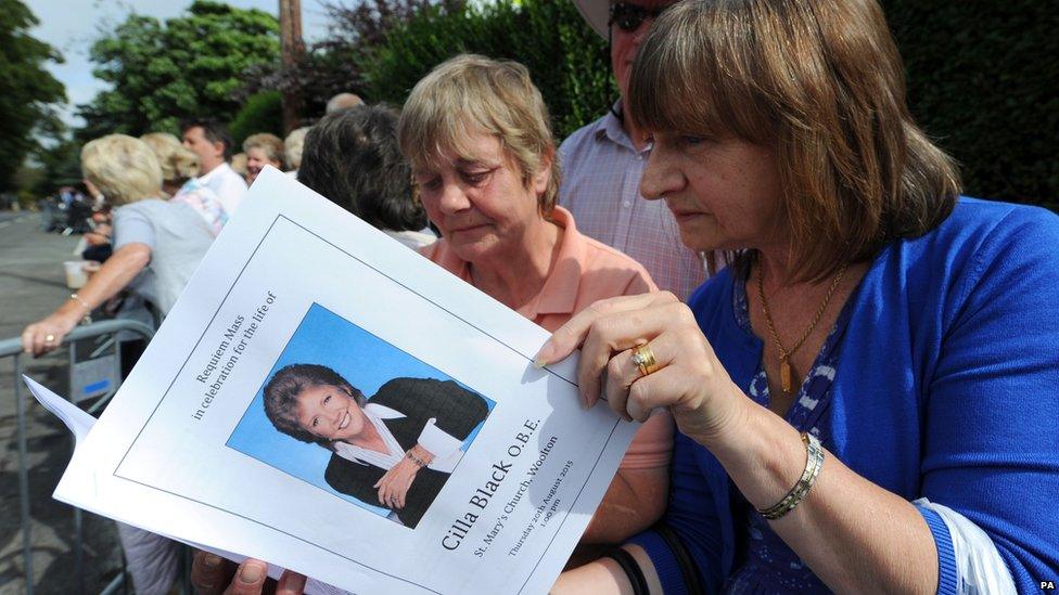 Members of the crowd read a copy of the order of service ahead of the funeral