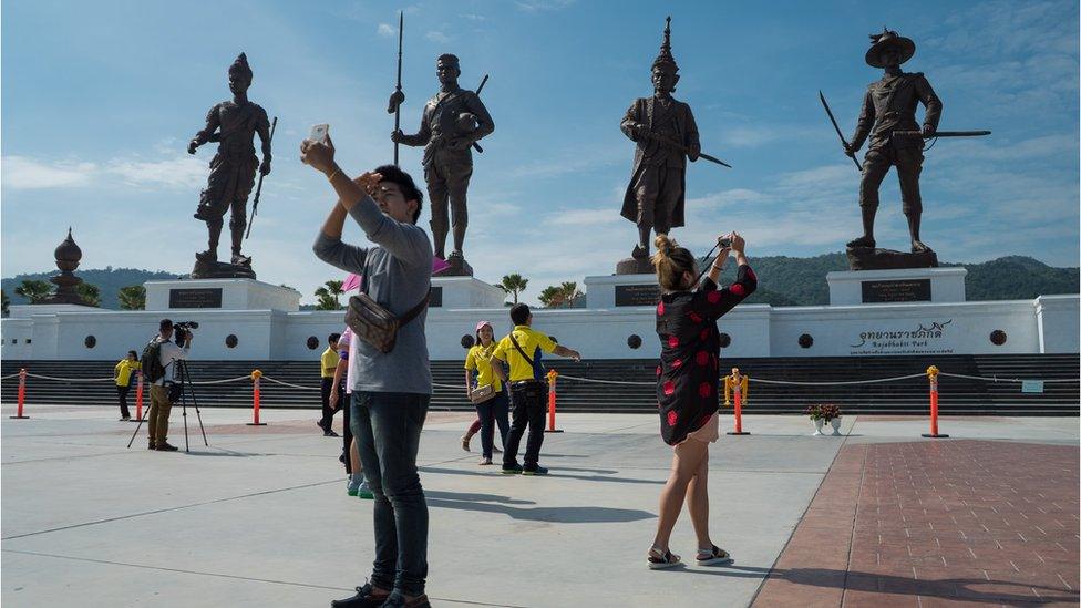 Statues of former Thai kings at Ratchapakdi park, with tourists in front of them, taking pictures