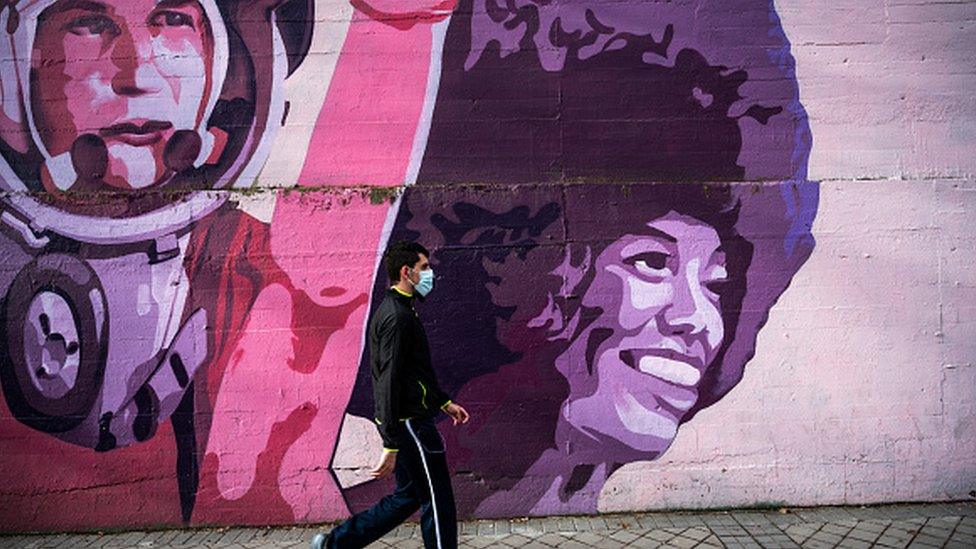 A man wearing a mask walks past a feminist mural in Madrid