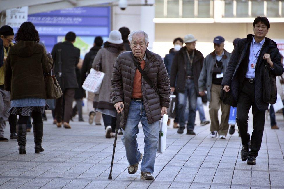 An elderly man walks with a stick