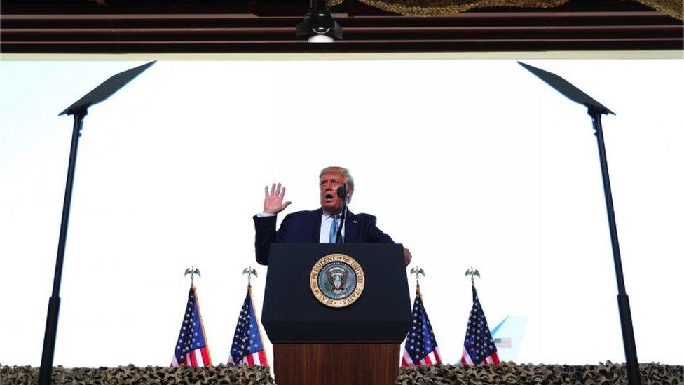 Donald Trump makes a speech with US flags in the background