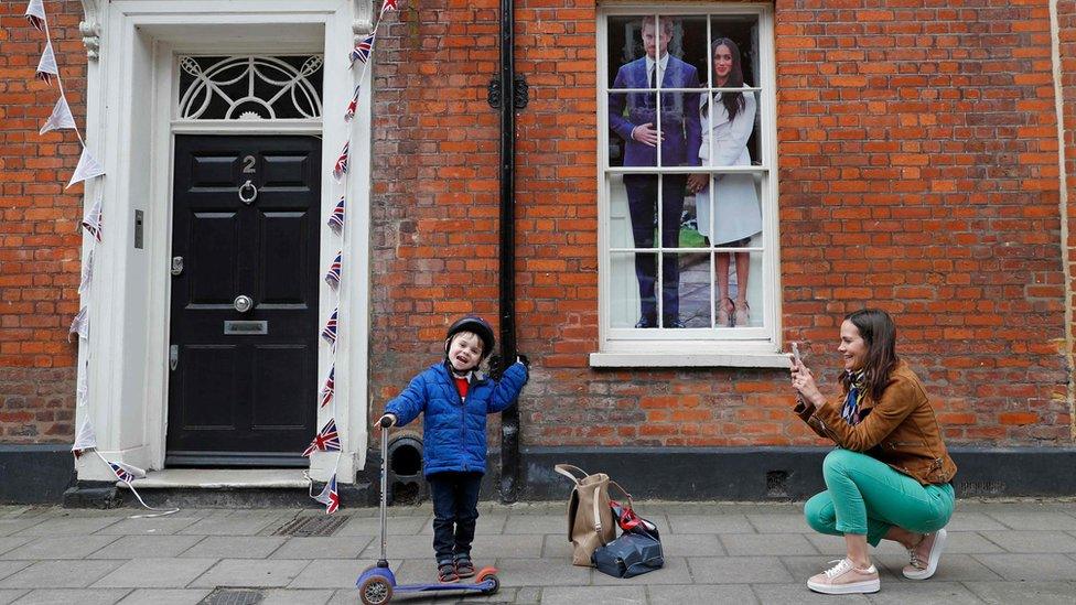 An image of Britain's Prince Harry and his US fiancée Meghan Markle is seen in a window as a woman photographs a child near Windsor Castle in Windsor