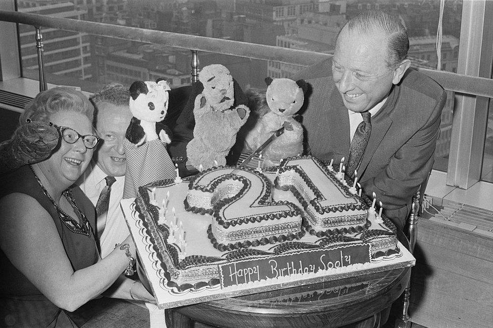 Harry Corbett and his wife Marjorie with Sooty, Sweep and Soo and a birthday cake on Sooty's 21st birthday in 1969