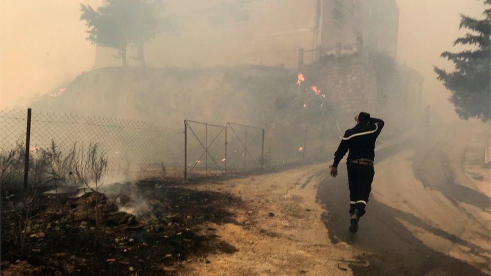 A civil protection rescue worker walks near smoke rising from a forest fire in Tizi Ouzou province